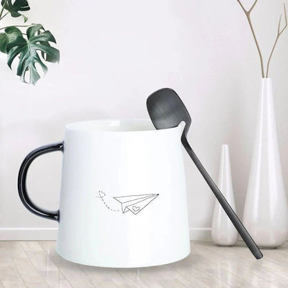 Black flatware spoon resting by its bent neck on the rim of a white mug