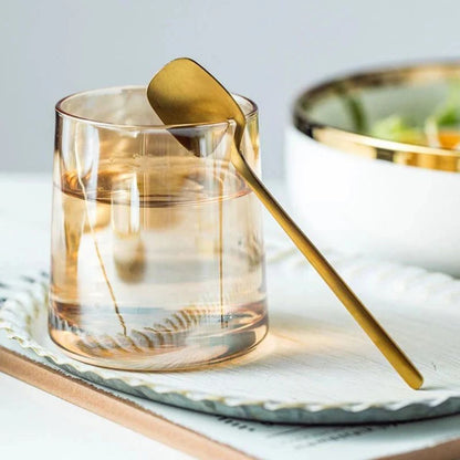 Gold flatware spoon resting on the rim of a glass tumbler