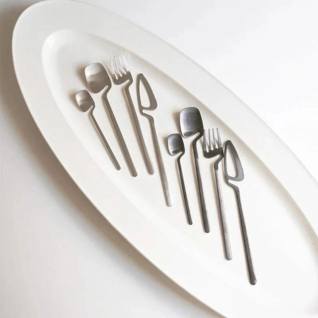 Two silver flatware sets laid out on an oval white platter