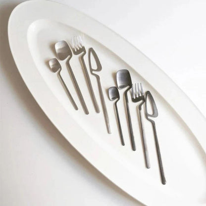 Two silver flatware sets laid out on an oval white platter
