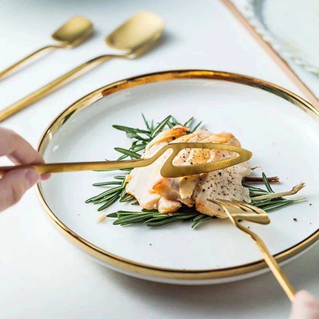 Gold flatware knife and fork cutting chicken on a gold-rimmed plate
