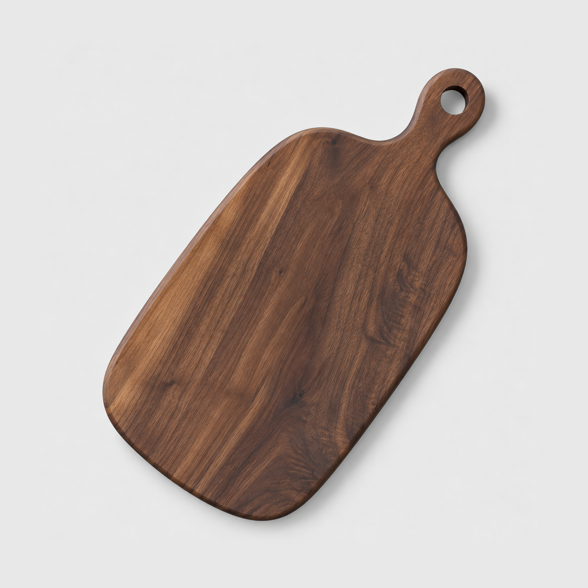 Large black walnut paddle cutting board with a handle and hang hole on a light gray background