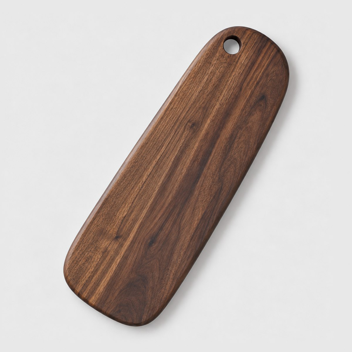 Long narrow black walnut cutting board with a hang hole on a light gray background
