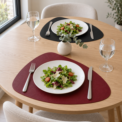Two Burgundy and Black placemats on a round light wood table in daylight, one burgundy side up and one black