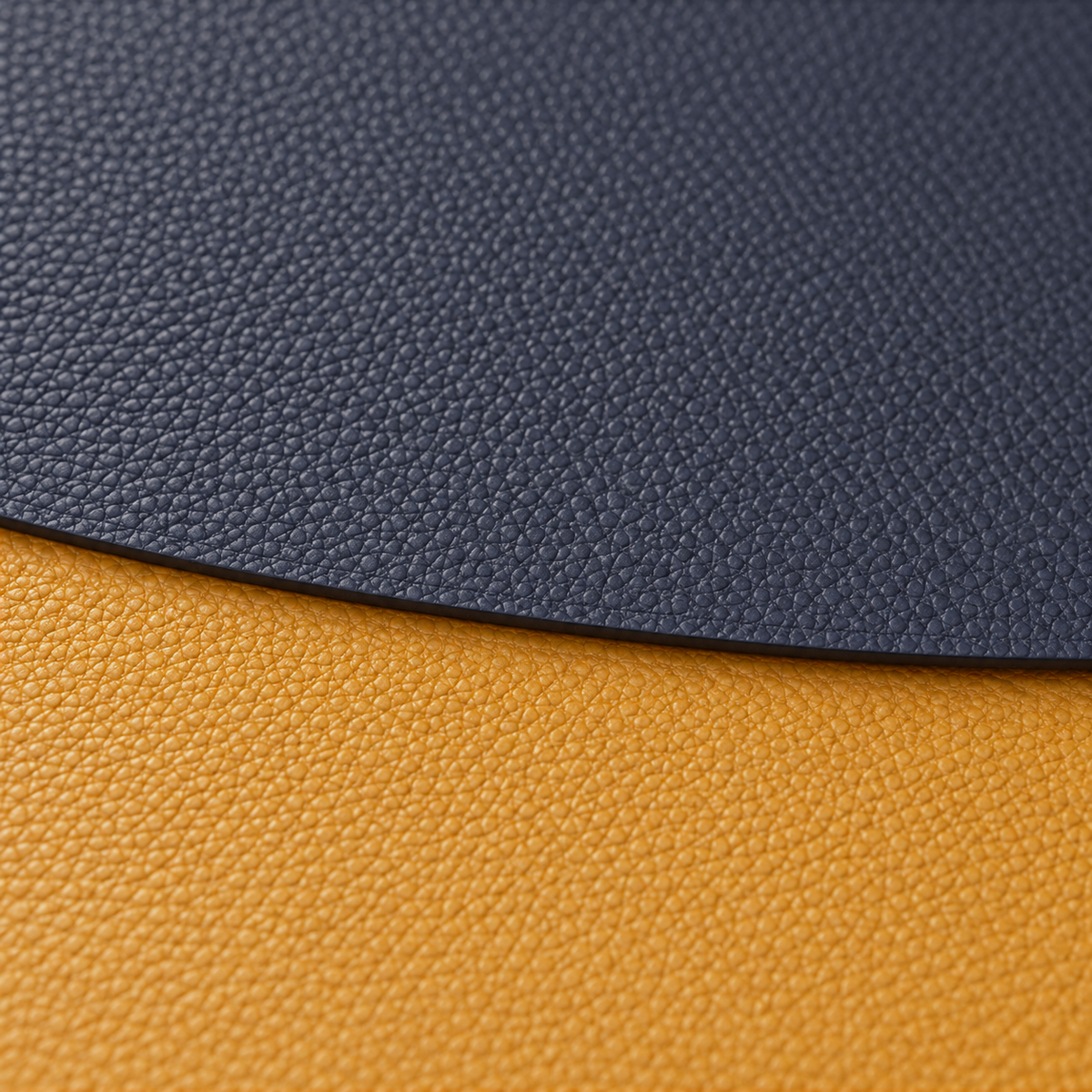 Close-up of the fine pebble grain and thin edge where a navy placemat overlaps a mustard one