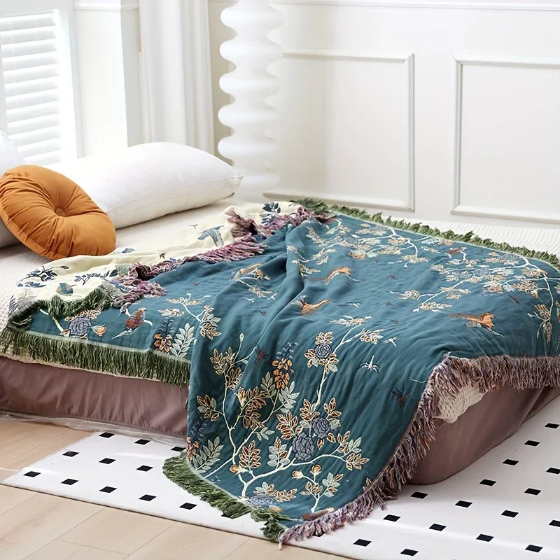 Teal cotton gauze blanket draped across a bed, flowering branches and birds on the teal face and the cream reverse turned back at the head