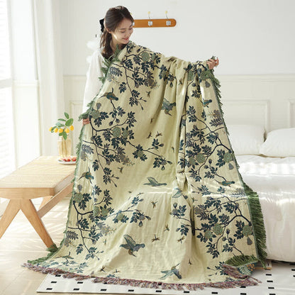 The cream reverse of the teal blanket held up full length, dark green branches and birds with a green fringe down both long sides