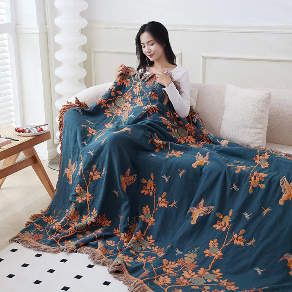 The dark blue reverse of the orange blanket over a woman on a cream sofa, orange branches, leaves and birds