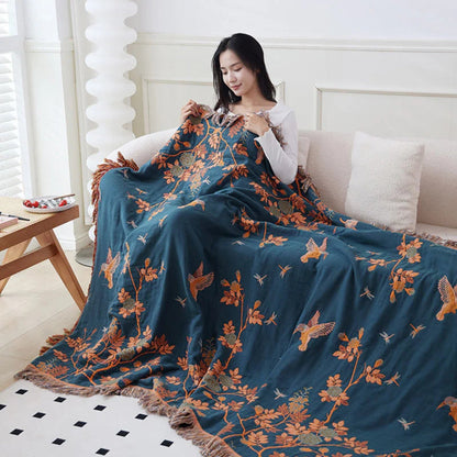 The dark blue reverse of the orange blanket over a woman on a cream sofa, orange branches, leaves and birds