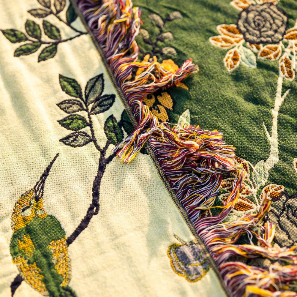 Close-up of the teal blanket's cream reverse beside its green face, the jacquard leaves and a multicolored fringe between them