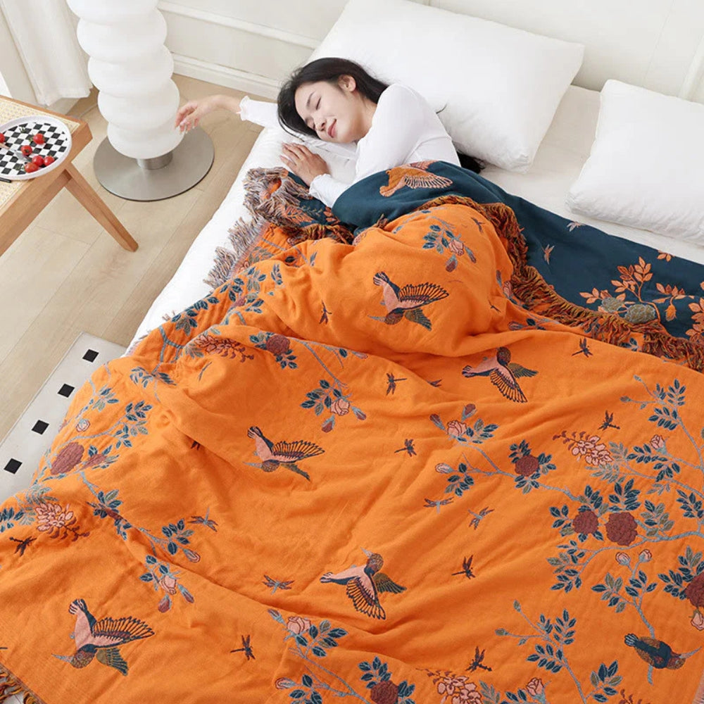 Orange bird and branch cotton blanket over a bed, the dark slate blue reverse folded back at the top with orange birds