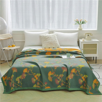Green ginkgo jacquard quilt spread over a bed, orange, pink and chartreuse leaves on long stems, the orange reverse showing at the head