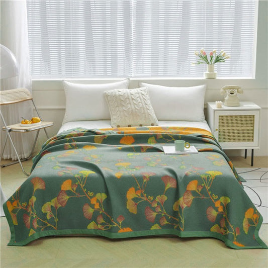 Green ginkgo jacquard quilt spread over a bed, orange, pink and chartreuse leaves on long stems, the orange reverse showing at the head