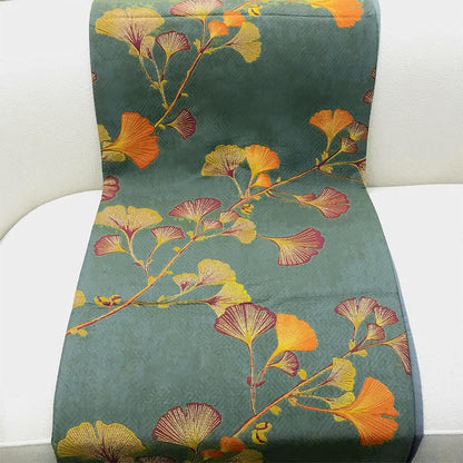 Green ginkgo quilt draped over a white sofa seat, woven fan-shaped leaves in orange, pink and chartreuse on a zigzag-textured green ground