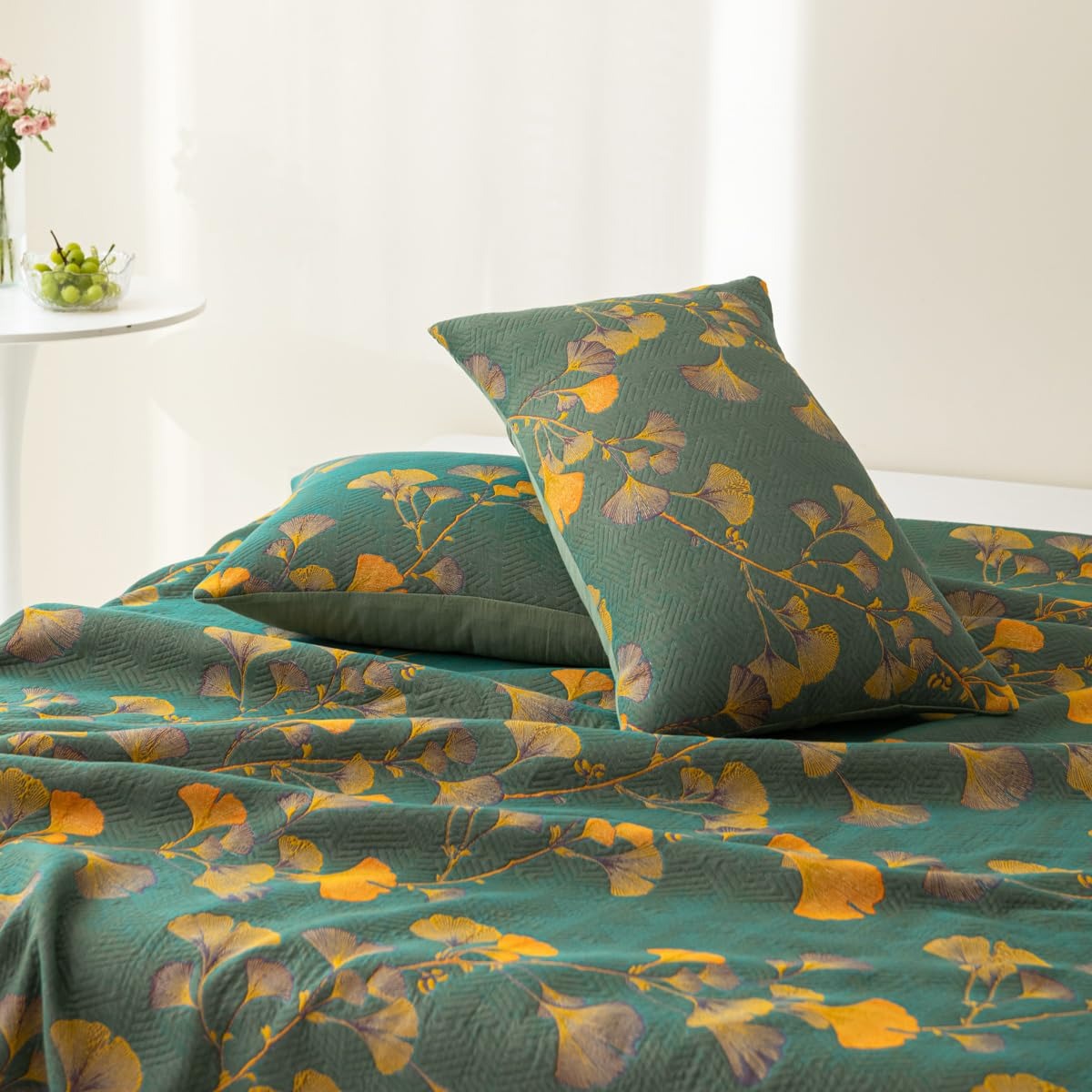 Two ginkgo pillowcases on a bed, gold and mauve leaves on a teal-green jacquard