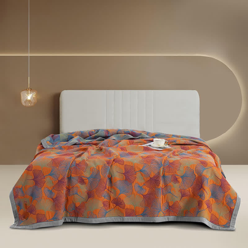 Blue and orange ginkgo leaf quilt spread over a bed, orange face up with the blue side at the head and a wide gray border