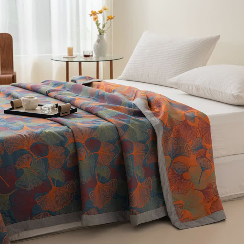 Ginkgo leaf quilt over the corner of a bed, the slate blue face on top and the orange face falling over the side