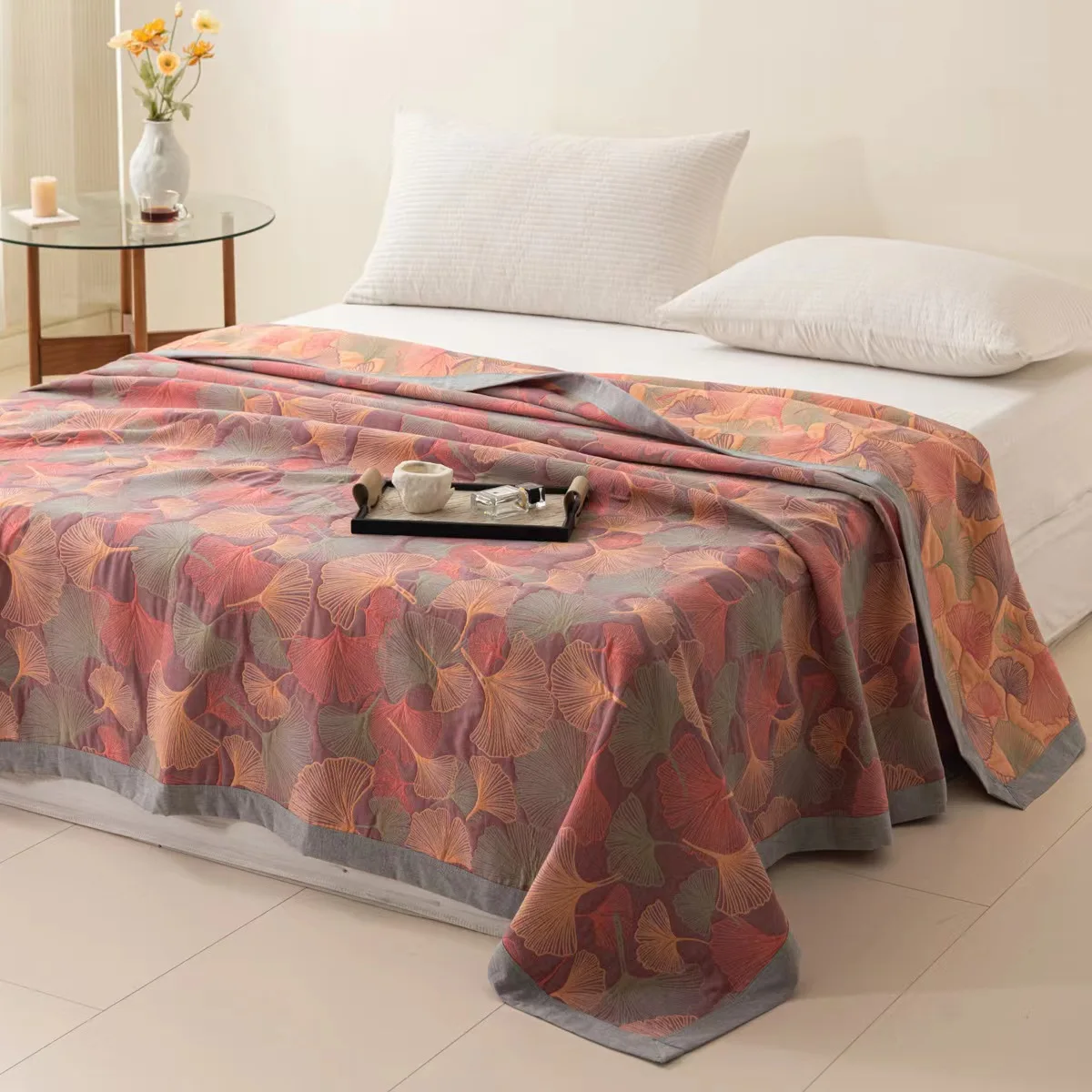 Rose ginkgo leaf quilt spread over a bed, orange, mauve and soft green leaves on a dusty coral-pink ground with a gray border