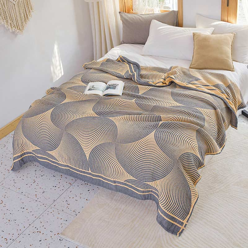 Yellow and charcoal tree ring cotton quilt spread over a bed, with its gray striped border band along the foot