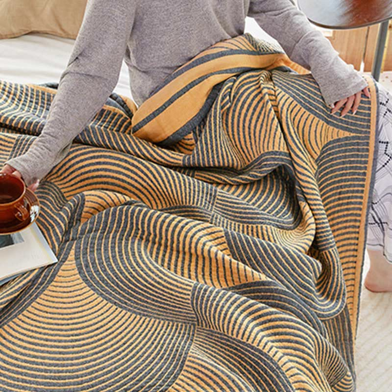 Yellow tree ring quilt pulled over a lap in bed, with a mug and an open book at one side