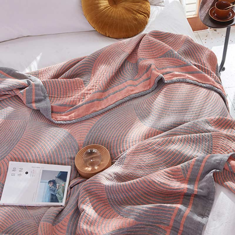 Coral and gray tree ring quilt draped over a bed, its edge turned back to show the solid coral reverse of the border