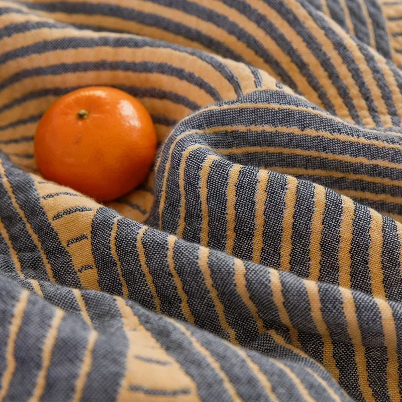 Macro of the woven charcoal and yellow stripes of the quilt's border, with a tangerine resting in a fold