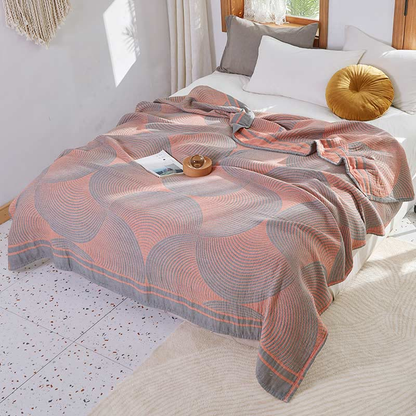 Coral and gray tree ring cotton quilt spread over a bed, with its gray striped border band along the foot