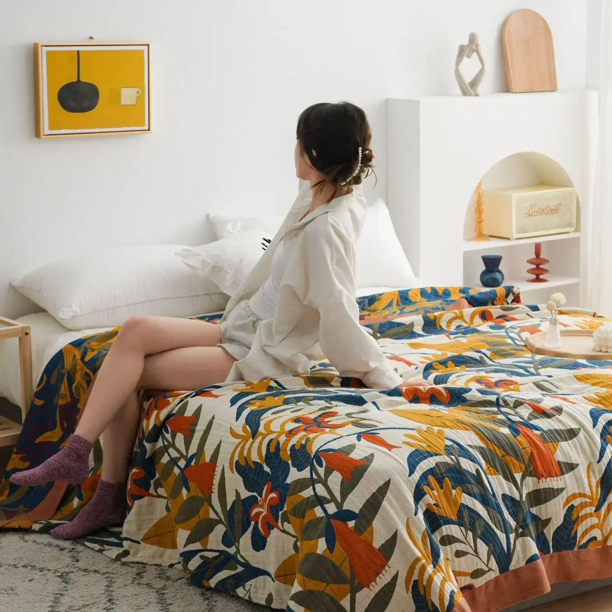 Woman sitting on the edge of a bed covered with the goldenrod floral quilt, its crinkled cotton gauze texture showing
