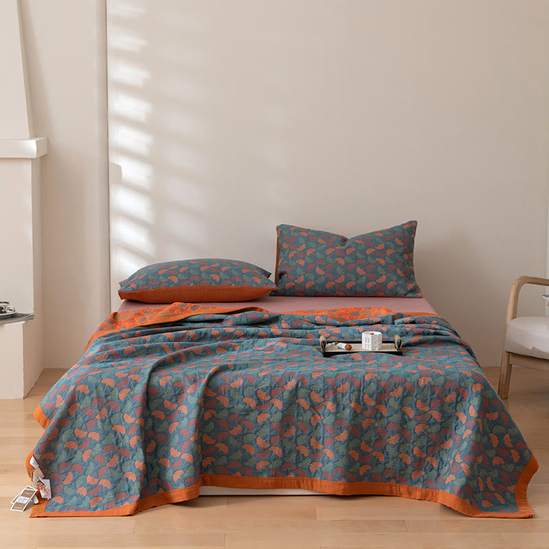 Teal ginkgo leaf cotton quilt spread over a bed seen from the front, the orange border along the hem and matching pillowcases