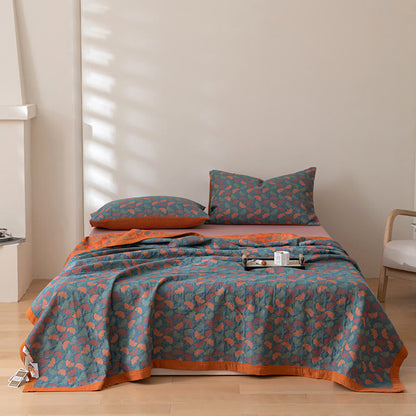 Teal ginkgo leaf cotton quilt spread over a bed seen from the front, the orange border along the hem and matching pillowcases