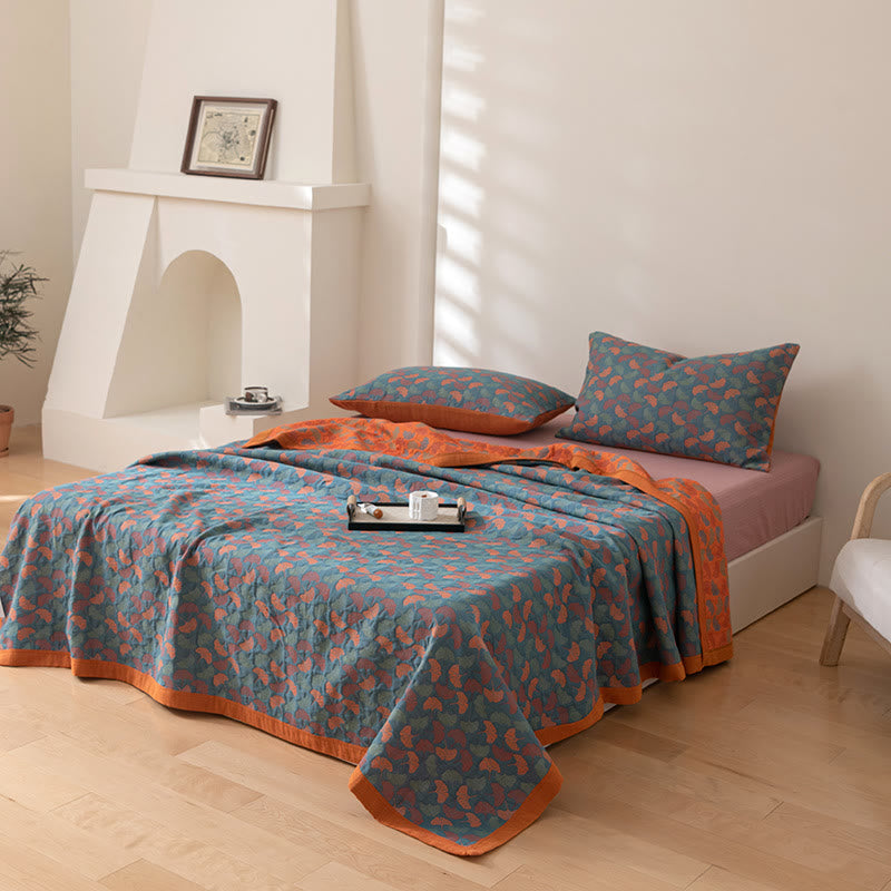 Teal ginkgo leaf cotton quilt spread over a bed with the orange reverse folded back at the head and matching pillowcases