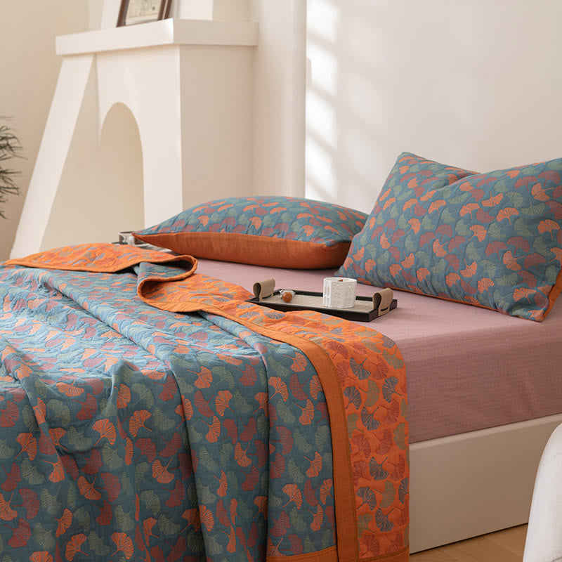 Corner of the reversible quilt on a bed, the teal leaf face over the side and the orange leaf reverse folded along the top