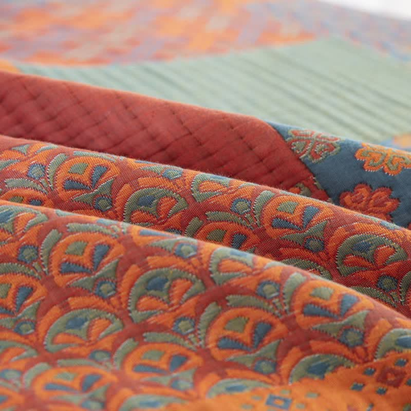 Close-up of the woven fanned scallop pattern in orange, green and blue, folded beside a rust channel-quilted block