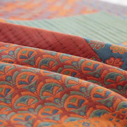 Close-up of the woven fanned scallop pattern in orange, green and blue, folded beside a rust channel-quilted block