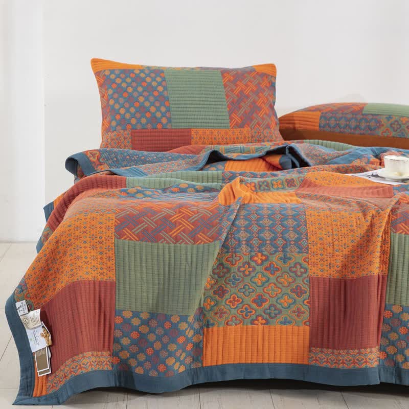 Closer view of the patchwork quilt over a bed, showing the four-petal flower, basketweave and floret blocks beside channel-quilted orange and sage blocks
