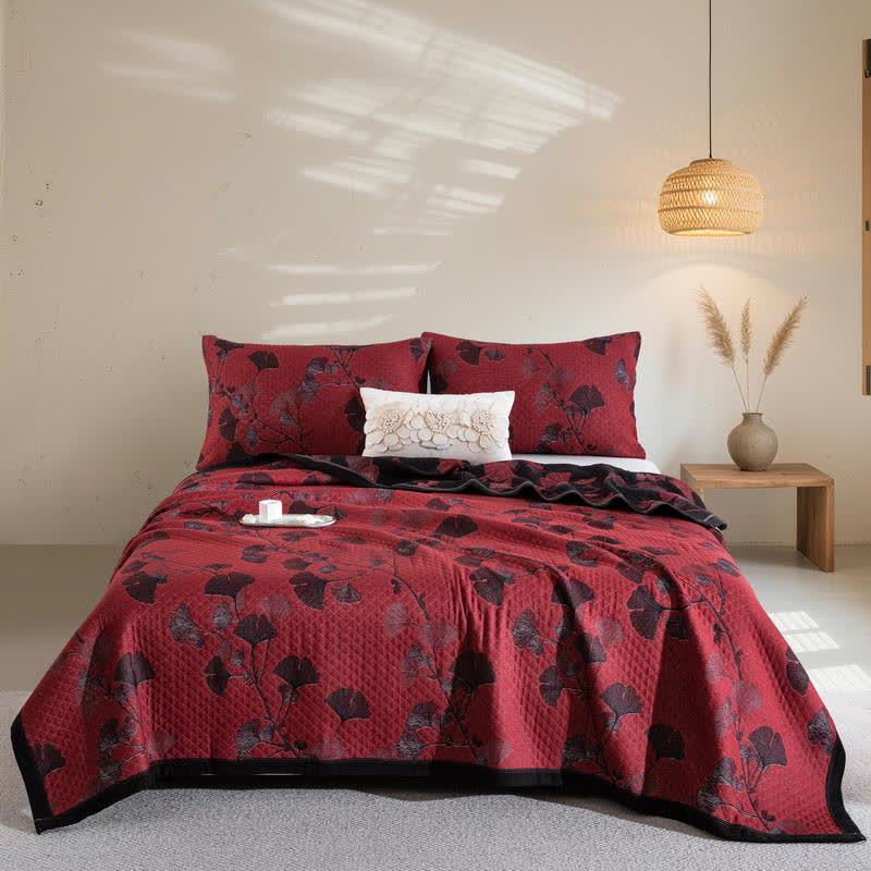 Red ginkgo branch quilt spread over a bed with matching pillowcases, black and maroon leaves and a black border