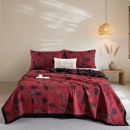 Red ginkgo branch quilt spread over a bed with matching pillowcases, black and maroon leaves and a black border