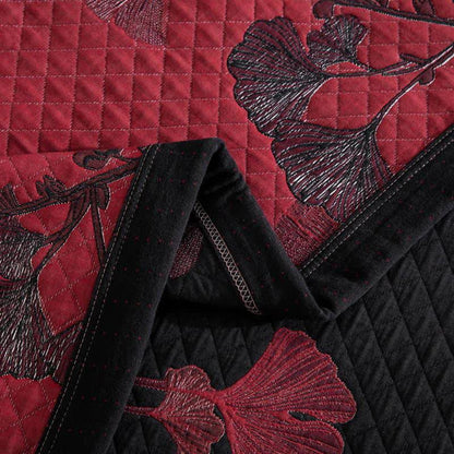 Close-up of the red quilt folded at the corner, diamond stitching and black ginkgo leaves, with the black reverse and border band