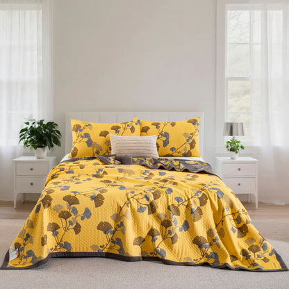 Yellow ginkgo branch quilt spread over a bed, straight on, with matching pillowcases, brown and slate blue leaves and a charcoal border