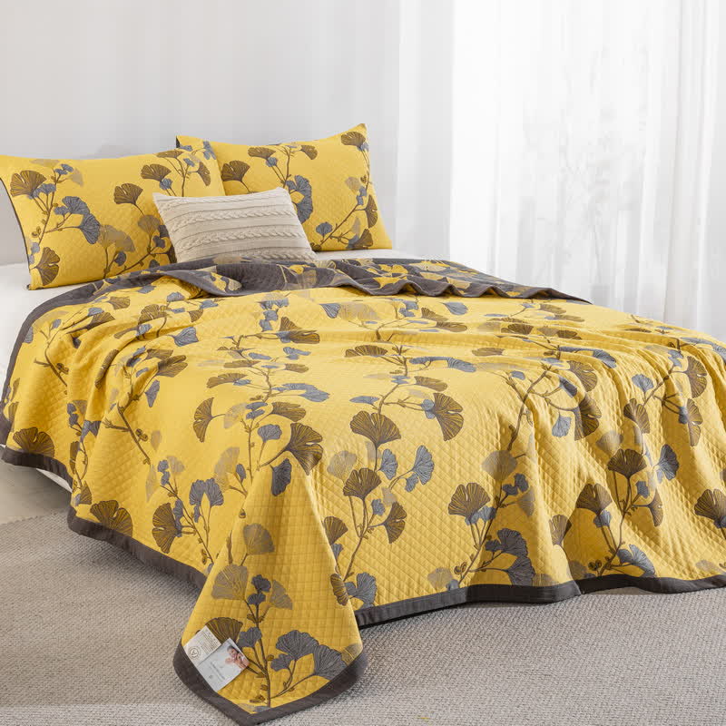 Yellow ginkgo quilt on a bed at an angle, the corner falling toward the floor, with the charcoal reverse at the head