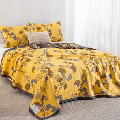 Yellow ginkgo quilt on a bed at an angle, the corner falling toward the floor, with the charcoal reverse at the head