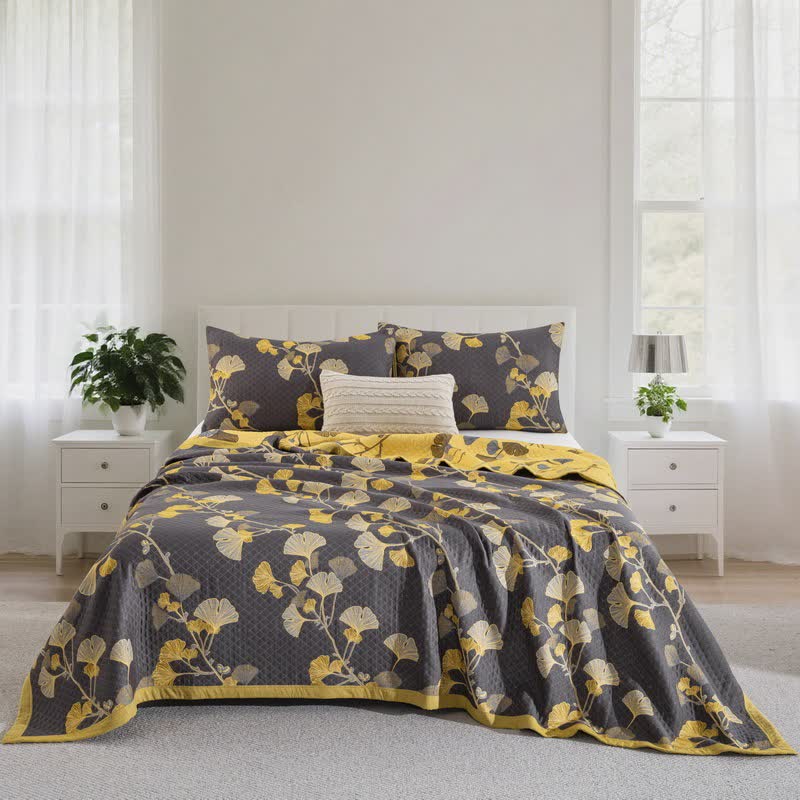Charcoal gray ginkgo branch quilt spread over a bed with matching pillowcases, yellow and cream leaves and a yellow reverse at the foot
