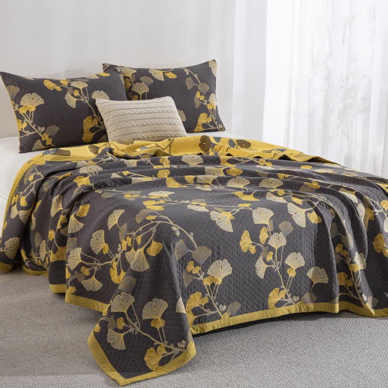 Reversible ginkgo quilt on a bed, the charcoal face on top and the yellow reverse folded back along the side and edge