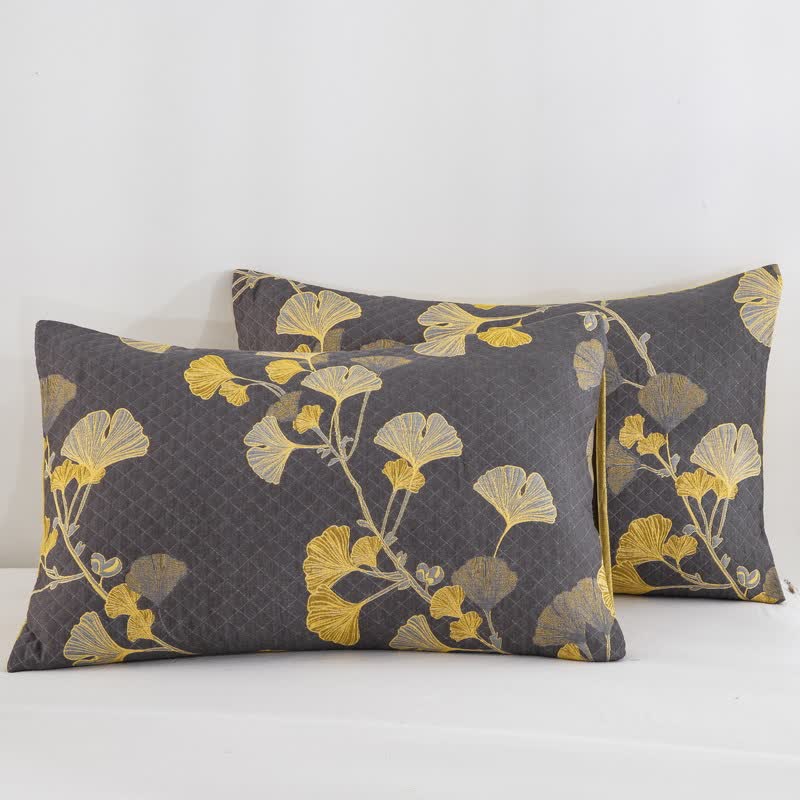 Two charcoal gray quilted pillowcases with yellow ginkgo branches and a thin yellow piped edge