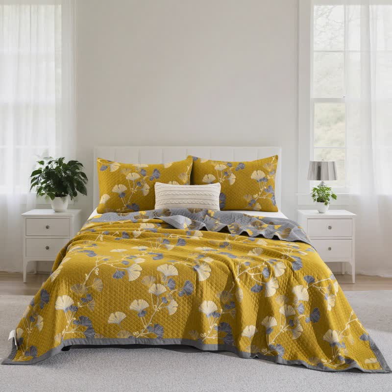 Mustard ginkgo leaf quilt with gray and cream leaves spread over a bed in a bright room, the gray reverse along the head