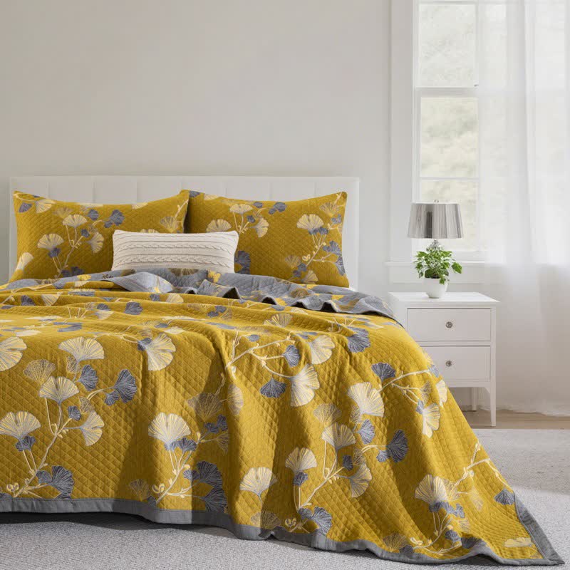 Mustard ginkgo branch quilt on a bed with matching pillowcases, cream and slate blue leaves and a gray border