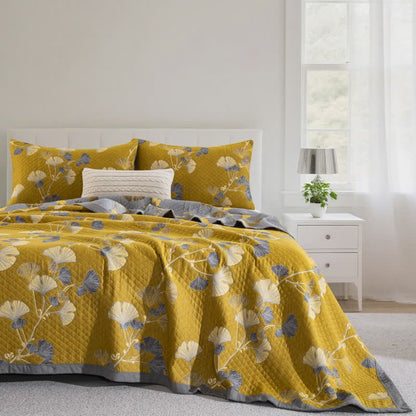 Mustard ginkgo branch quilt on a bed with matching pillowcases, cream and slate blue leaves and a gray border
