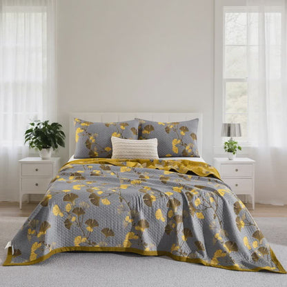 Gray ginkgo leaf quilt with mustard leaves spread over a bed between two white nightstands, matching pillowcases at the head