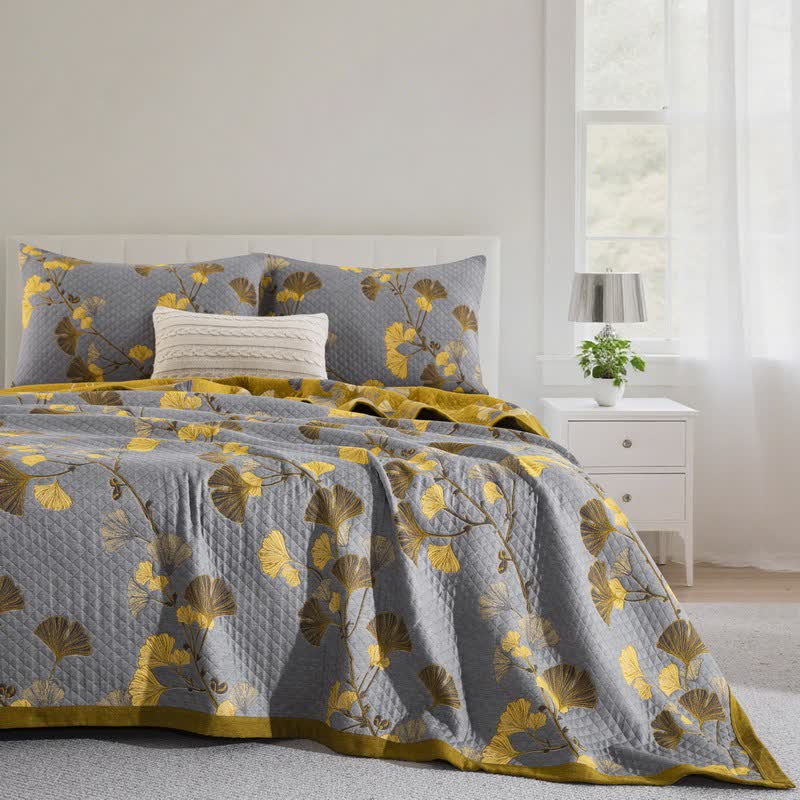 Gray ginkgo quilt with yellow and olive leaves on a bed, matching pillowcases and a mustard border