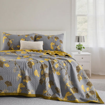 Gray ginkgo quilt with yellow and olive leaves on a bed, matching pillowcases and a mustard border